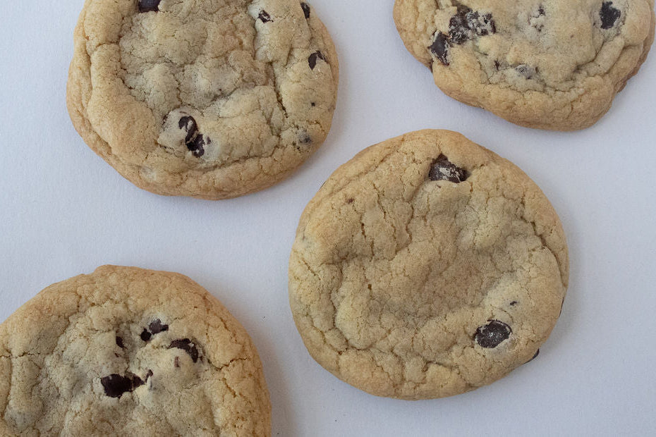 This image presents a delectable array of chocolate chip cookies, freshly baked and displayed on a simple white background. The cookies appear soft and chewy, with a golden-brown crust that suggests a delightful texture.